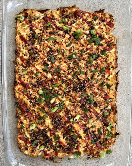 Salmon sushi bake in a casserole dish with furikake topping and sriracha drizzle