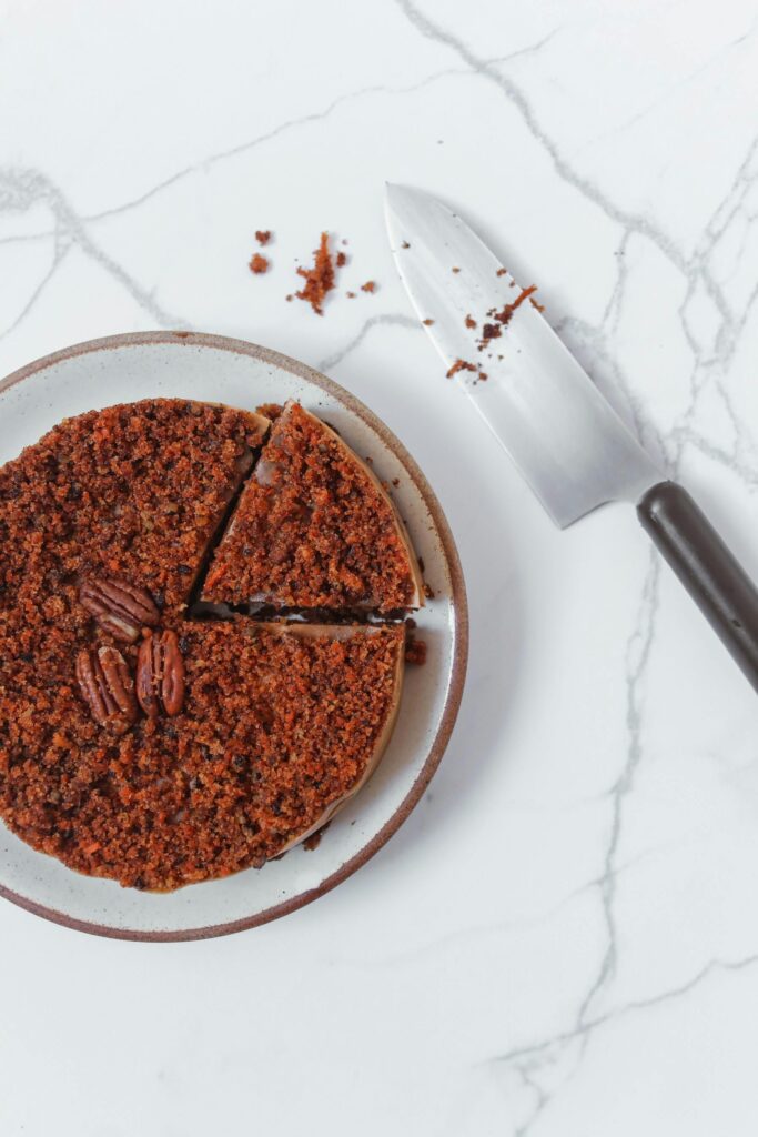 A slice of pecan pie cheesecake on a plate, topped with caramelized pecans and drizzled with caramel sauce.